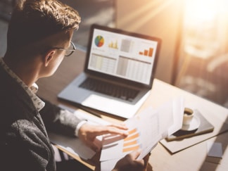Man looking at laptop screen and printout of a graph